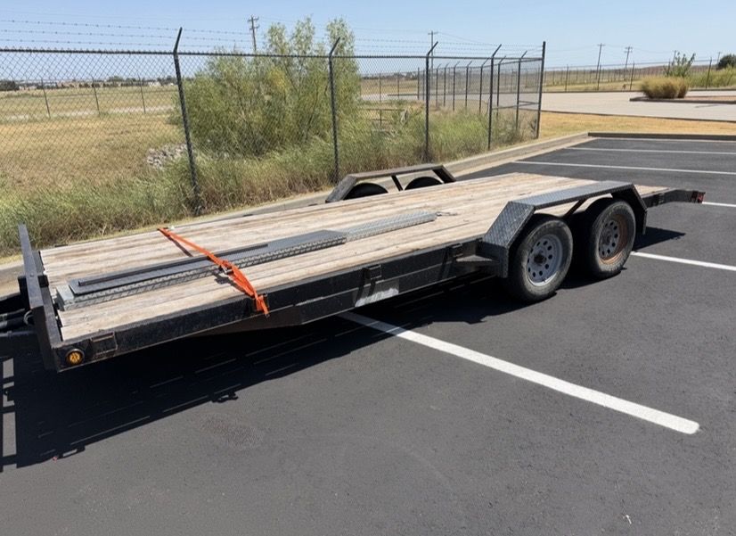 Drive over trailer fenders installed on a flatbed car hauler with tandem axles and loading ramps on the deck